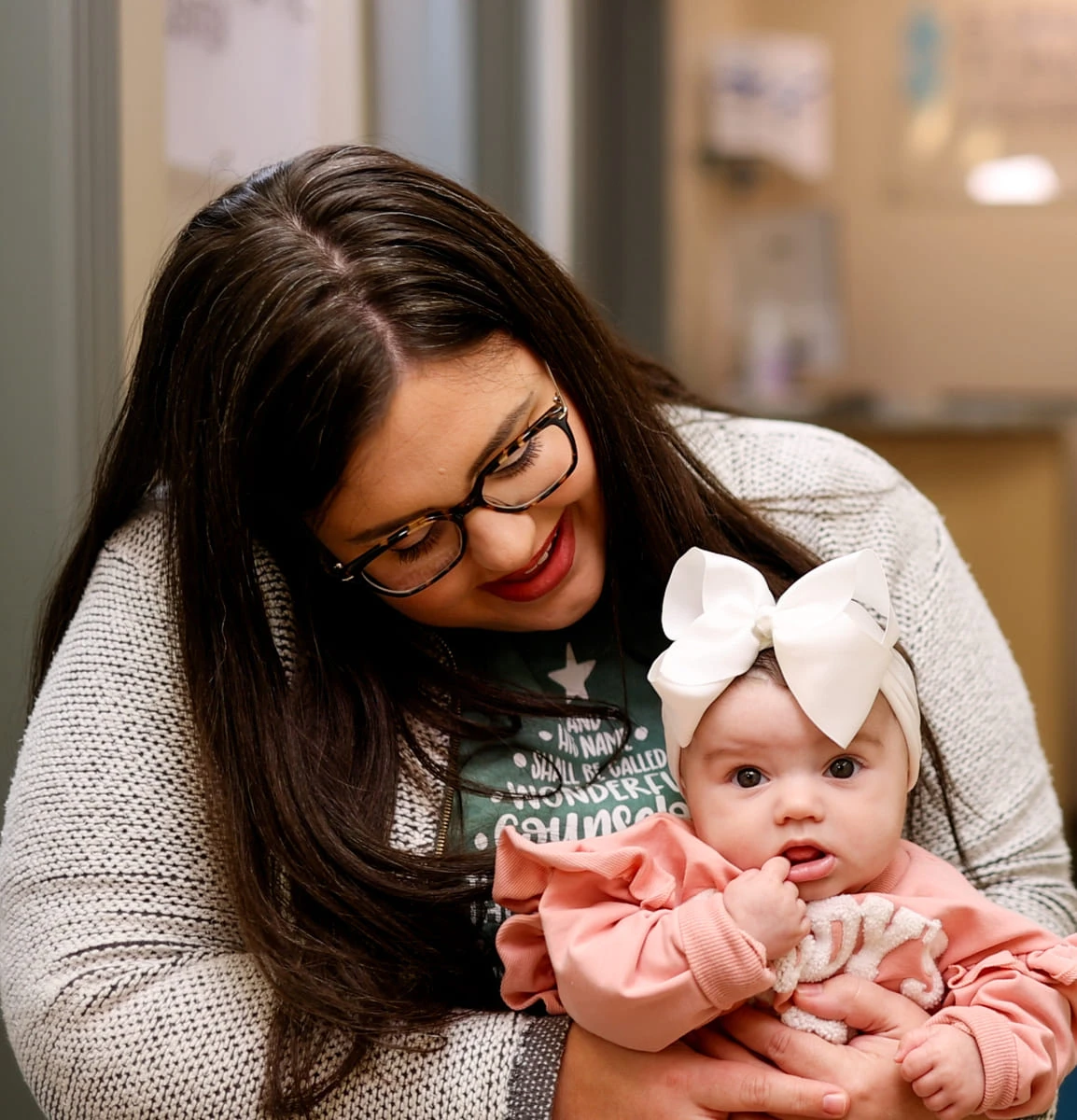 Smiling mom holding her baby girl in a white bow at the Alabama Tongue-Tie Center